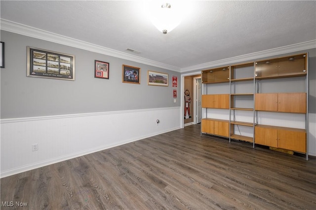 unfurnished room with visible vents, crown molding, dark wood-type flooring, wainscoting, and a textured ceiling