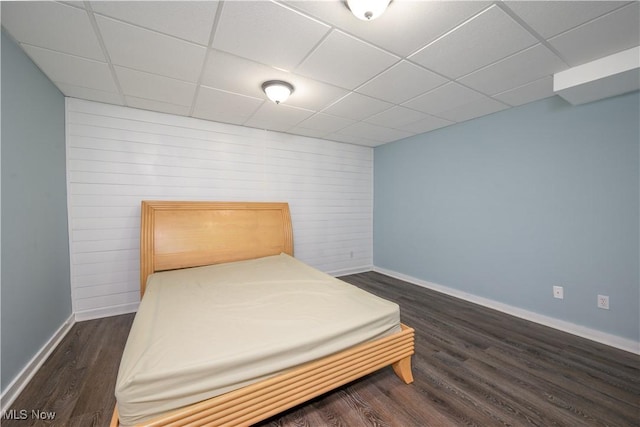 bedroom with a drop ceiling, baseboards, and dark wood-style flooring