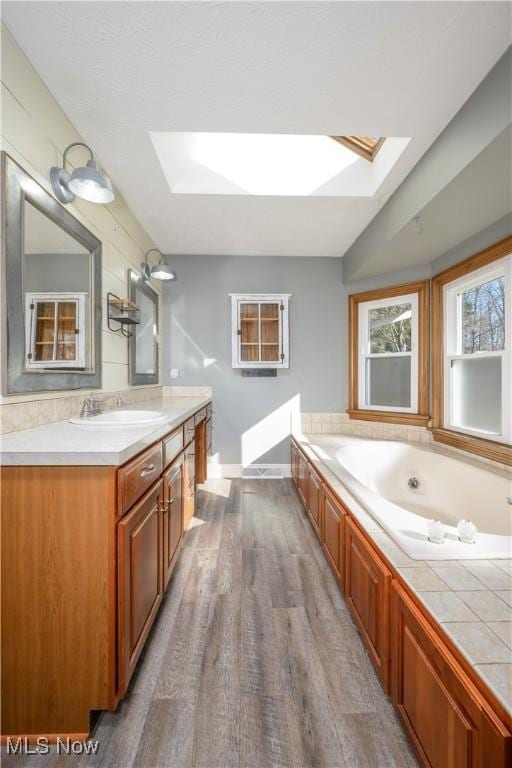 full bath featuring lofted ceiling with skylight, wood finished floors, baseboards, a bath, and vanity