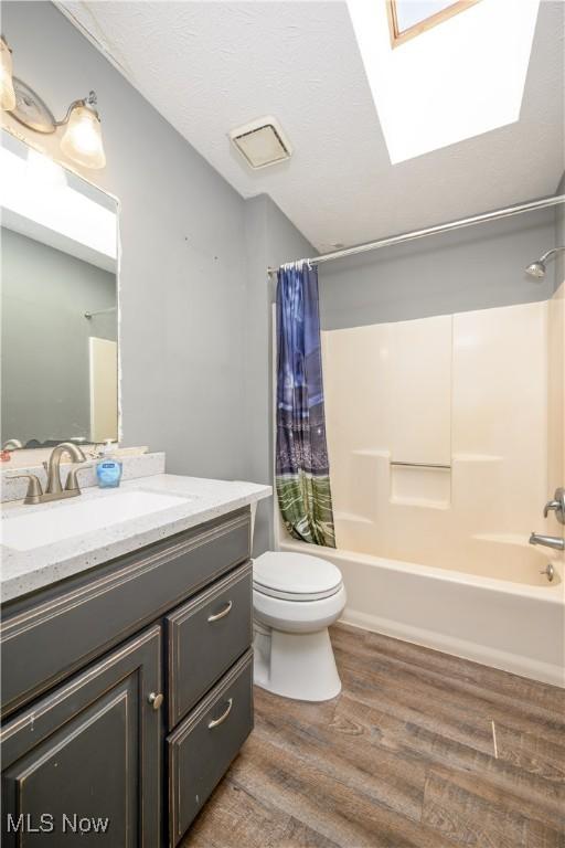 full bath with vanity, wood finished floors, a skylight, shower / bath combo with shower curtain, and toilet