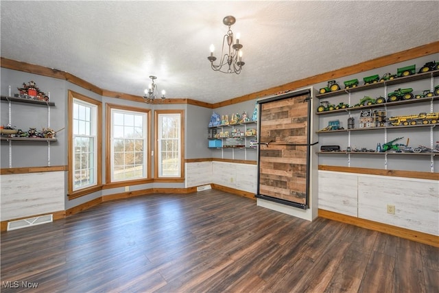 unfurnished dining area featuring visible vents, a notable chandelier, a textured ceiling, wood finished floors, and wainscoting