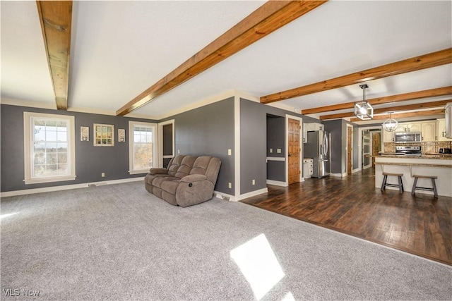 living area featuring beam ceiling, baseboards, dark colored carpet, and dark wood-type flooring