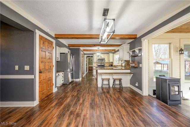 kitchen with dark wood finished floors, beam ceiling, a peninsula, and stainless steel appliances