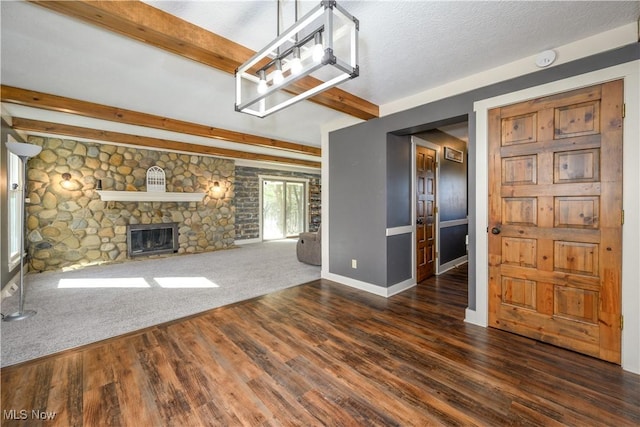 unfurnished living room with baseboards, beamed ceiling, a fireplace, wood finished floors, and a textured ceiling