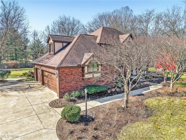 view of side of property featuring driveway, an attached garage, brick siding, and roof with shingles