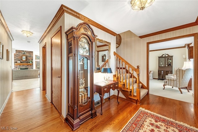 hallway featuring wallpapered walls, baseboards, light wood-type flooring, stairs, and ornamental molding