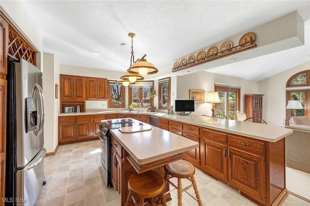 kitchen with a peninsula, light countertops, brown cabinetry, and appliances with stainless steel finishes