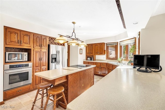 kitchen featuring a sink, a center island, appliances with stainless steel finishes, brown cabinetry, and light countertops