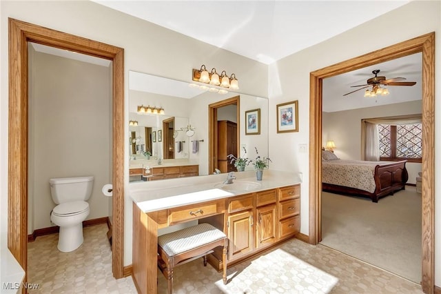 ensuite bathroom featuring vanity, baseboards, ceiling fan, toilet, and connected bathroom