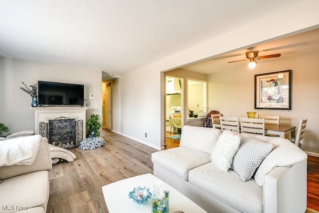 living room with a ceiling fan, wood finished floors, baseboards, and a fireplace