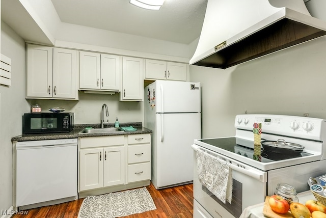 kitchen with dark countertops, a sink, range hood, white appliances, and dark wood-style flooring