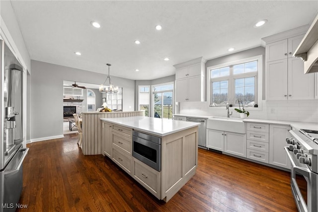 kitchen with a glass covered fireplace, dark wood-style floors, a center island, stainless steel appliances, and decorative backsplash