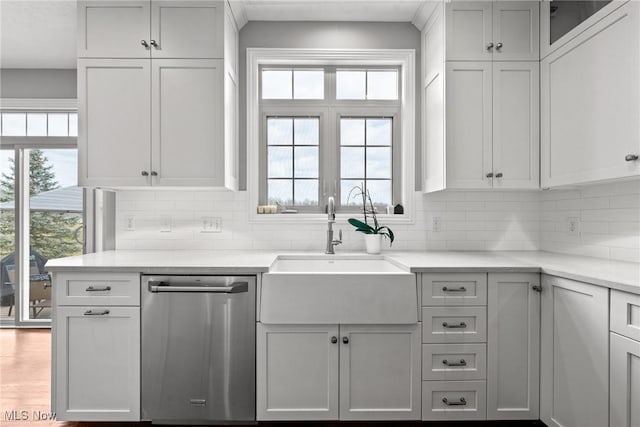 kitchen featuring wood finished floors, a sink, decorative backsplash, light countertops, and stainless steel dishwasher