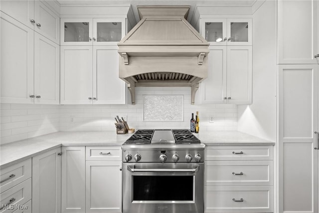 kitchen featuring high end range, custom range hood, white cabinets, glass insert cabinets, and backsplash