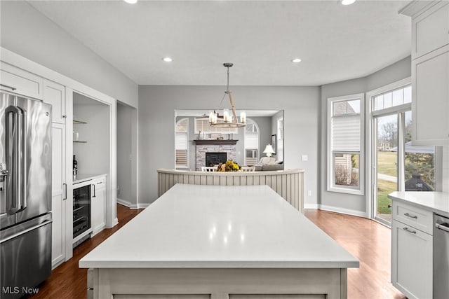 kitchen with a kitchen island, wine cooler, a stone fireplace, appliances with stainless steel finishes, and light countertops