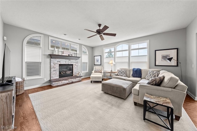 living room featuring a fireplace, baseboards, a ceiling fan, and wood finished floors