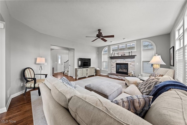 living area with a stone fireplace, a healthy amount of sunlight, dark wood-style flooring, and ceiling fan