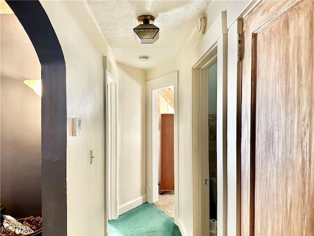 corridor featuring arched walkways, baseboards, a textured ceiling, and carpet