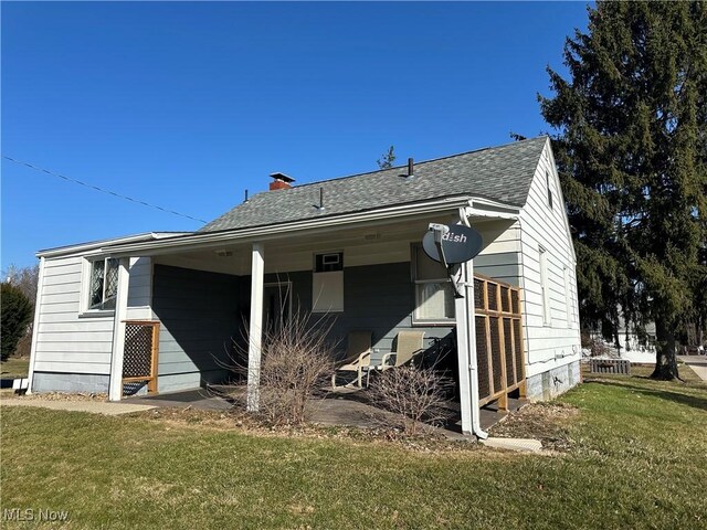 rear view of property featuring a yard, roof with shingles, and a chimney