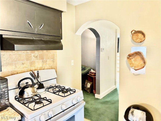 kitchen featuring carpet, white range with gas cooktop, arched walkways, under cabinet range hood, and backsplash