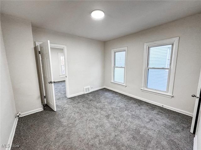 unfurnished room featuring baseboards, visible vents, and dark carpet