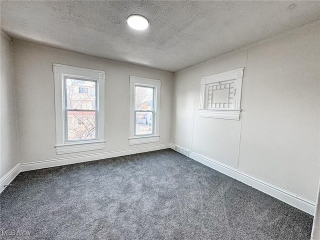 spare room featuring baseboards, a textured ceiling, and dark carpet