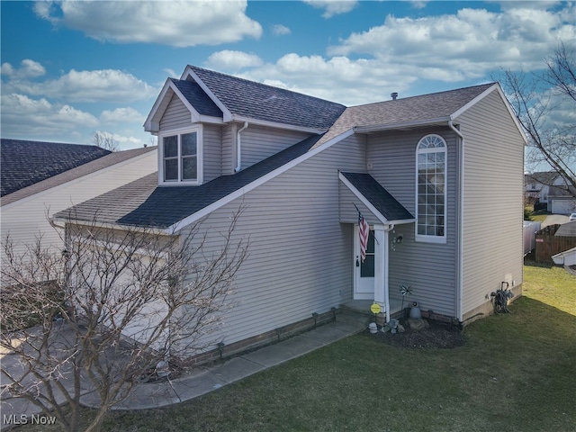 view of front of house with entry steps, a front yard, and a shingled roof