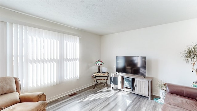 living area with visible vents, baseboards, a textured ceiling, and wood finished floors