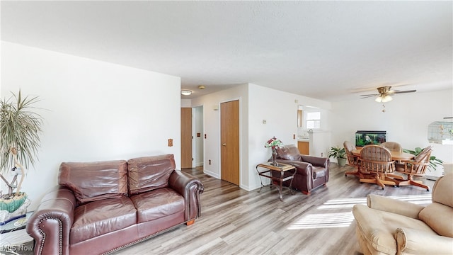 living area featuring baseboards, light wood-type flooring, and ceiling fan