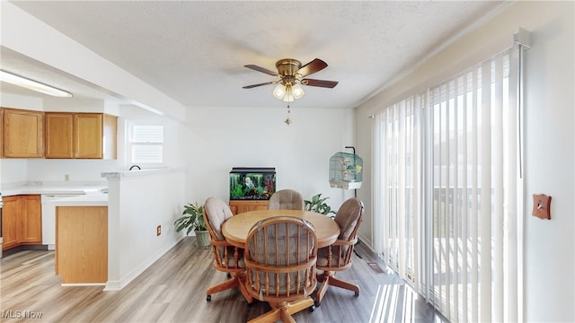 dining room featuring light wood-type flooring, baseboards, a textured ceiling, and a ceiling fan