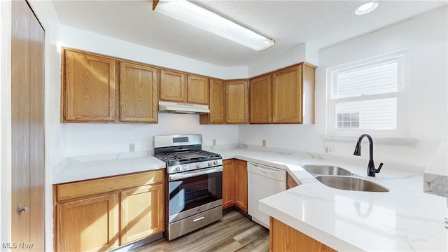 kitchen with under cabinet range hood, light stone counters, white dishwasher, stainless steel gas stove, and a sink