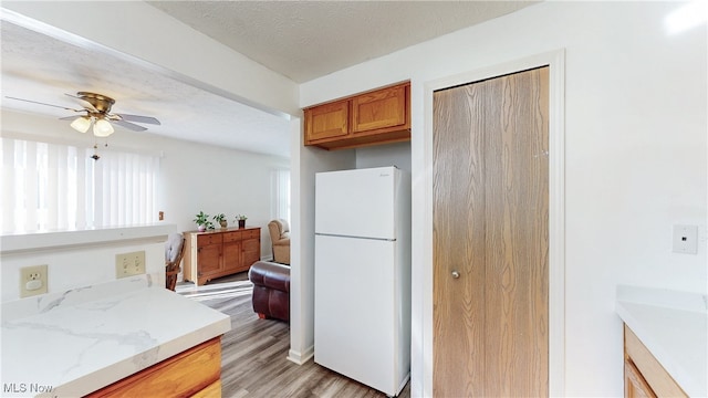 kitchen featuring ceiling fan, light wood-style flooring, freestanding refrigerator, brown cabinetry, and a textured ceiling