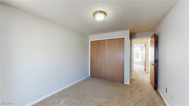 unfurnished bedroom featuring a closet, light carpet, a textured ceiling, and baseboards