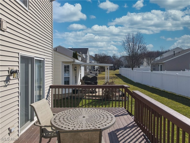 deck featuring a residential view, a lawn, outdoor dining area, and fence