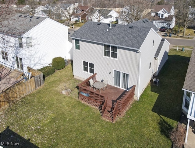 rear view of property with a lawn, fence, roof with shingles, a wooden deck, and central AC unit