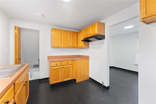 kitchen featuring baseboards, dark wood-style flooring, a sink, light countertops, and under cabinet range hood