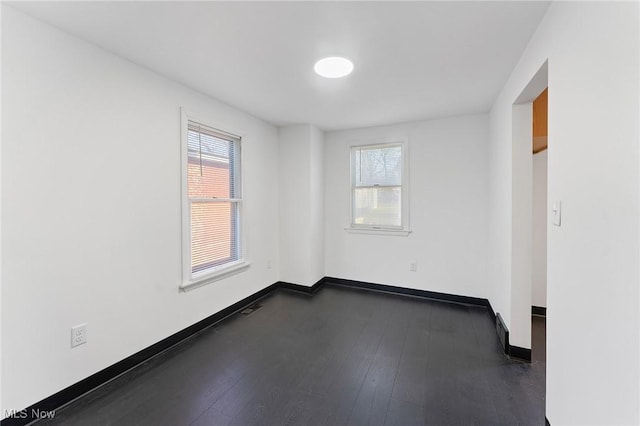 spare room with dark wood finished floors, visible vents, and baseboards