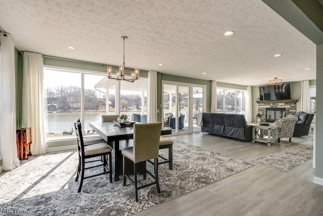 dining space with wood finished floors, an inviting chandelier, a fireplace, recessed lighting, and a water view