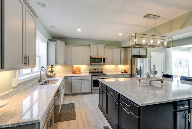 kitchen with a sink, stainless steel appliances, light stone counters, and a kitchen island