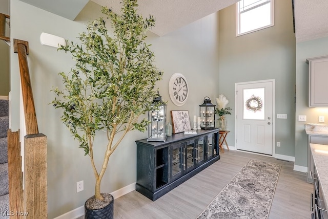 foyer entrance featuring baseboards, a textured ceiling, light wood-style flooring, and stairs