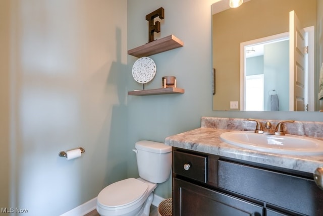 half bathroom featuring toilet, vanity, and baseboards