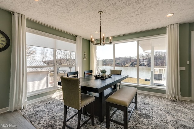 dining area with baseboards, wood finished floors, an inviting chandelier, and a water view