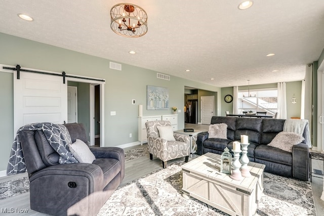 living room featuring visible vents, a barn door, light wood-style floors, and an inviting chandelier