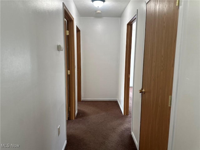 hallway featuring baseboards, carpet, and a textured ceiling