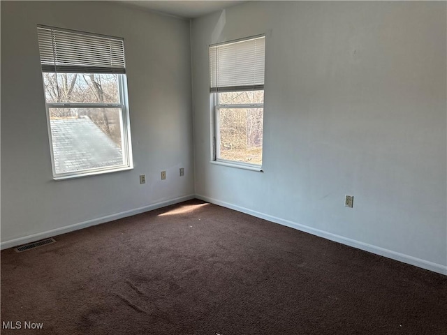 unfurnished room with dark colored carpet, baseboards, and plenty of natural light