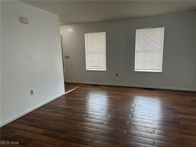 empty room with baseboards and dark wood-type flooring