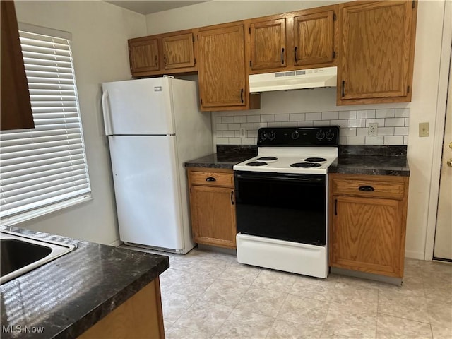 kitchen with electric range, under cabinet range hood, tasteful backsplash, dark countertops, and freestanding refrigerator