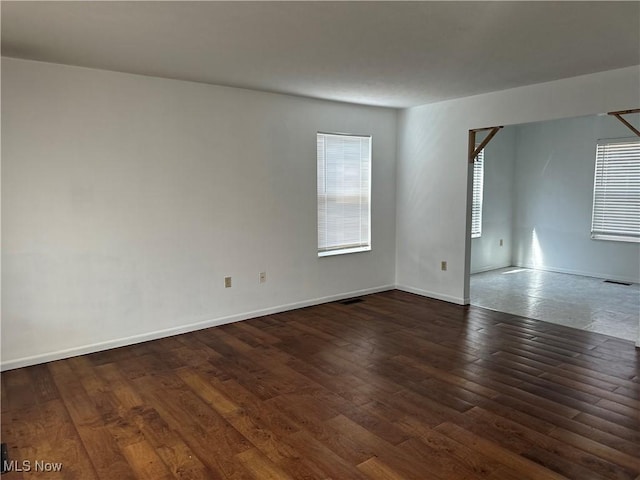 empty room featuring visible vents, baseboards, and dark wood-style floors