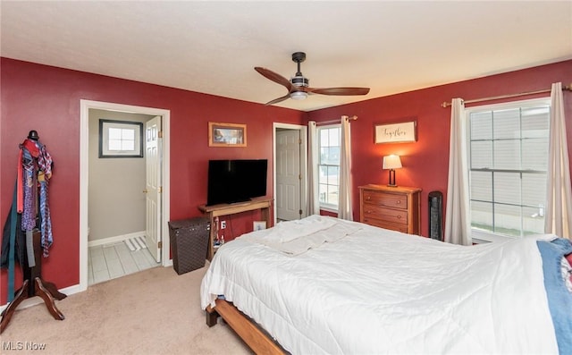 carpeted bedroom featuring ensuite bath, multiple windows, a ceiling fan, and baseboards