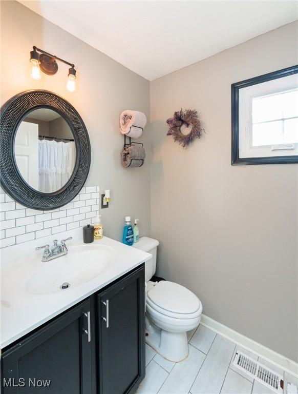 full bath featuring vanity, baseboards, visible vents, decorative backsplash, and toilet